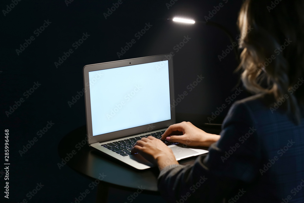 Woman working on laptop at table in evening Woman working on laptop at table in evening