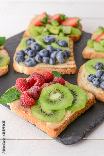 Tasty sandwiches with kiwi and berries on slate plate, closeup