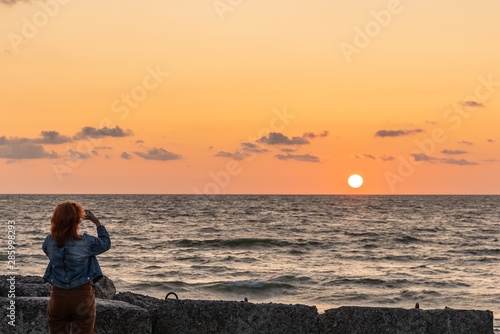 Young woman photographs a beautiful sunset on the sea © Igor