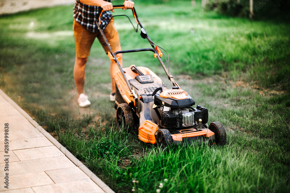 Fototapeta premium Gardening and landscaping concept - worker, gardener working with lawnmower and cutting grass in garden.