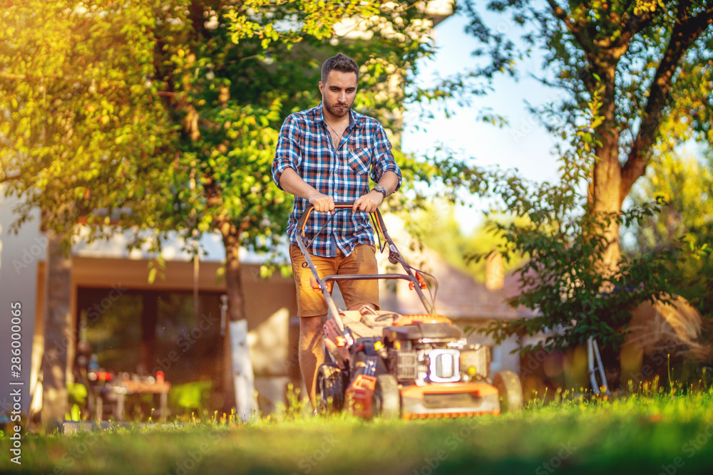 Portrait of handsome caucasian garden worker using a lawnmower in backyard garden Portrait of handsome caucasian garden worker using a lawnmower in backyard garden
