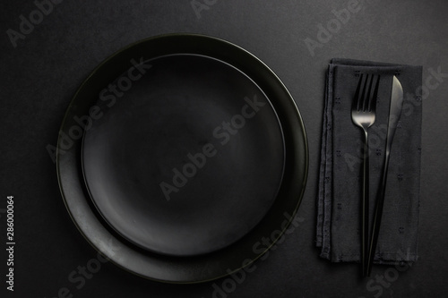 Black setting: plates, linen napkin and silverware on blfck background. Top view.