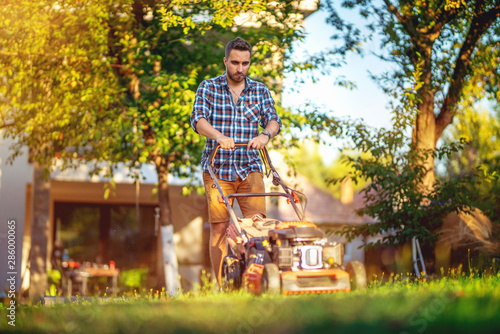 Portrait of handsome caucasian garden worker using a lawnmower in backyard garden