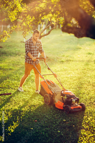 lawncare concept - garden maintainance with gardener working and cutting grass