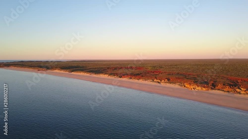 Scenic panoramic aerial drone view at sunset of flight high above ocean and remote beach in Western Australia, with rocky cliff coastline, summer sunny blue sky, horizon as background and copy space.