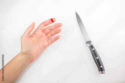 Accident wounded finger with blood and kitchen knife. Injured left hand finger with bleeding open cut on a white background