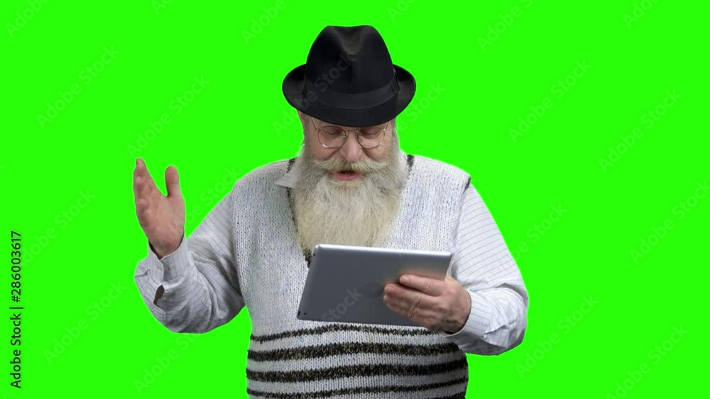 Aged man in eyeglasses using digital tablet. Green screen background. Old people and modern technology concept. Aged man in eyeglasses using digital tablet. Green screen background. Old people and modern technology concept.