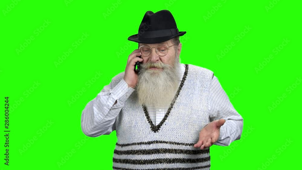 Angry senior man talking on mobile phone. Aged man arguing or having dispute with another person on cellphone. Green Chroma Key background. Angry senior man talking on mobile phone. Aged man arguing or having dispute with another person on cellphone. Green Chroma Key background.