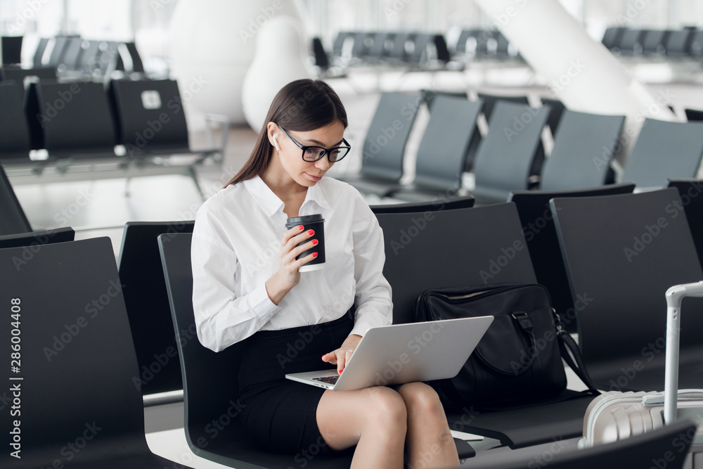 Young woman with coffee working on laptop sitting in a departure lounge of airport Young woman with coffee working on laptop sitting in a departure lounge of airport