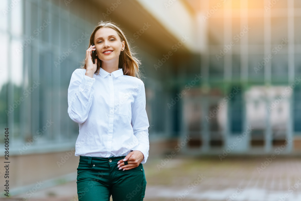Young famale calling on a smartphone. Attractive businesswoman talking by phone. Office building Background. Technology internet and happy people concept. Young famale calling on a smartphone. Attractive businesswoman talking by phone. Office building Background. Technology internet and happy people concept.