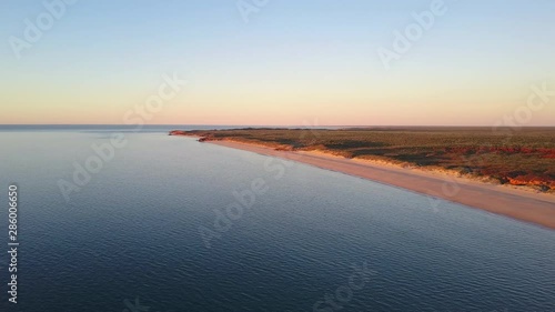 Scenic panoramic aerial drone view at sunset of flight high above ocean and remote beach in Western Australia, with rocky cliff coastline, summer sunny blue sky, horizon as background and copy space.