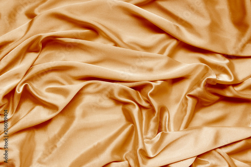 gold beautiful satin fabric draped with soft folds, silk cloth background, close-up, copy space