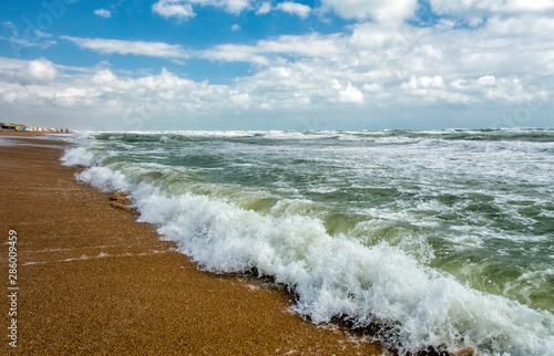 Scenic vertical landscape of sandy Black Sea beach by Anapa resort, Russia. Stormy waves splashing against beach sand on blue sky and clouds background on sunny summer day. Sea surf at storm. photo