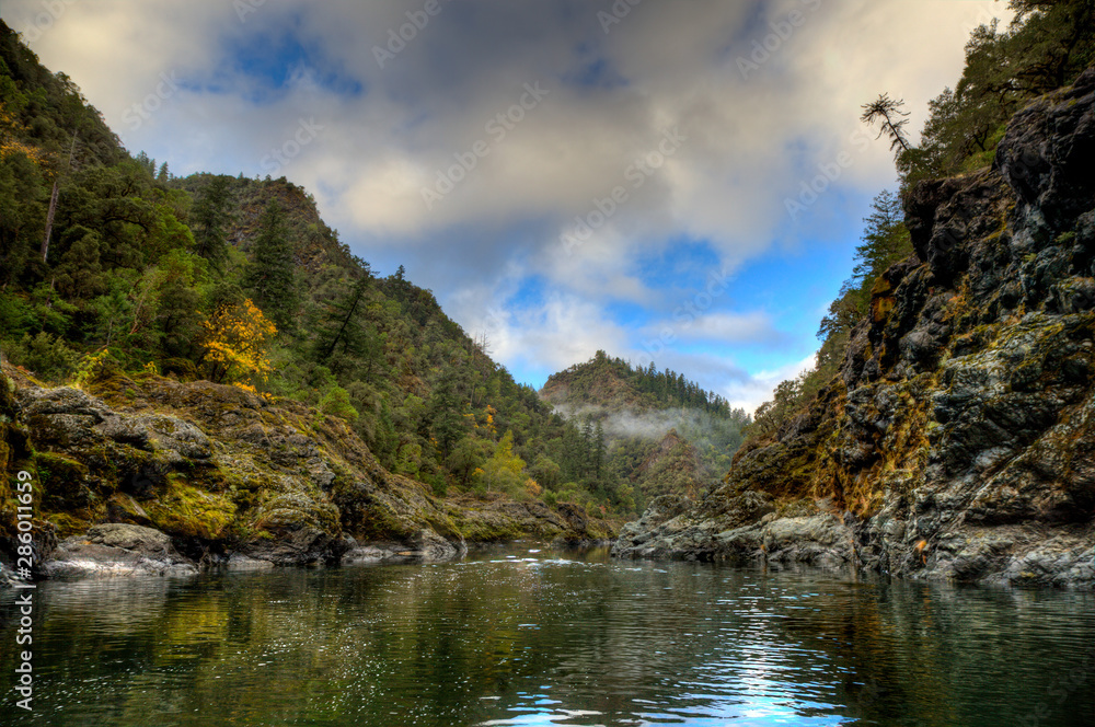 Calm and rocky section of the rogue river with a perfect pine forest and mountain in the background Calm and rocky section of the rogue river with a perfect pine forest and mountain in the background