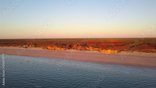 Scenic panoramic aerial drone view at sunset of flight high above ocean and remote beach in Western Australia, with rocky cliff coastline, summer sunny blue sky and horizon as background and copy spac