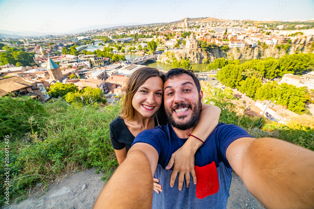 happy tourist couple taking selfie in Tbilisi with aerial view of old Tbilisi, Georgia. backpacker traveling in Caucasus 