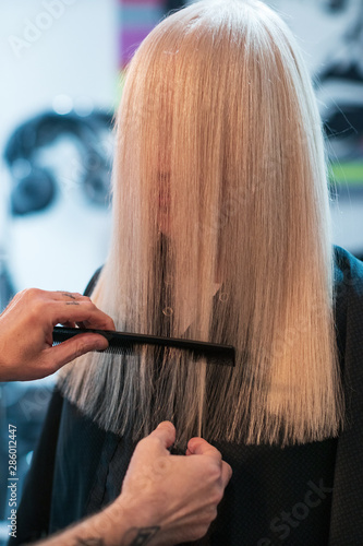 Close up barber's hands trimming the ends of long blonde hair with the scissors and the comb photo