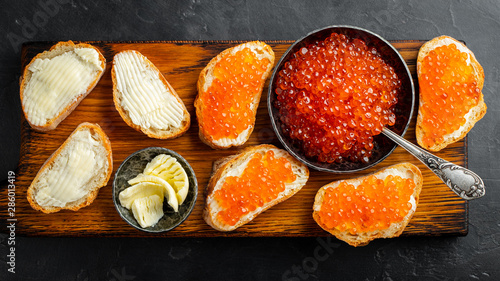 Close-up red caviar in bowl and Sandwiches on wooden cutting board on black background. Top view. Flat lay