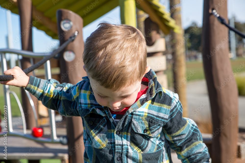 Obraz premium A little boy carefully practices walking across the swing bridge on the playground fort 