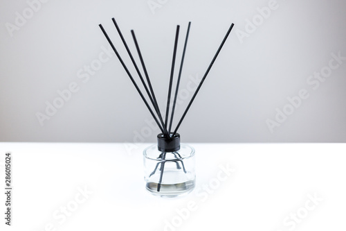 Aromatizer or perfume stick. Aromatic air freshener in a transparent glass bottle with black reeds on a white table