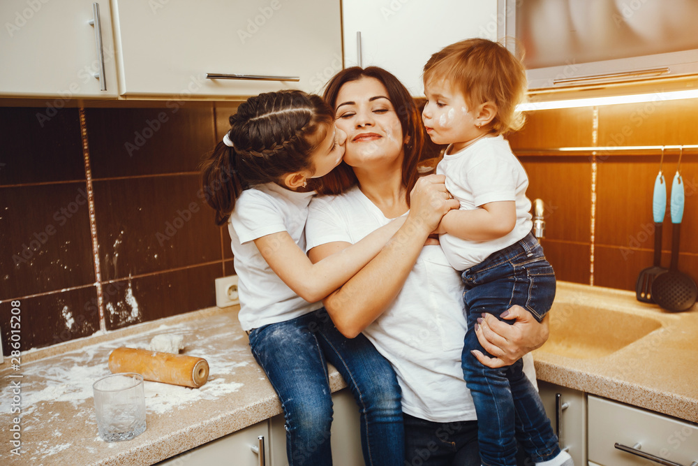 a young mother in a white t-shirt stands in the kitchen and works with flour along with her children a young mother in a white t-shirt stands in the kitchen and works with flour along with her children