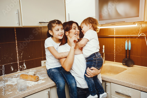 a young mother in a white t-shirt stands in the kitchen and works with flour along with her children