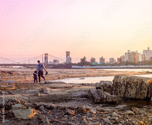 A father with his daughter watching the sunset on a waterfront in front of the river.