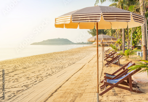 Row of empty wooden beach chairs with parasols on tropical sandy beach in the morning  relax leisure summer holidays concept 