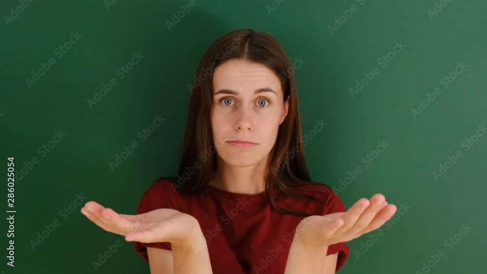 Pretty female with long hair, shrugs shoulders, being doubtful about making serious decision, feels uncertain, isolated over green background. Hesitation and confusion. Pretty female with long hair, shrugs shoulders, being doubtful about making serious decision, feels uncertain, isolated over green background. Hesitation and confusion.