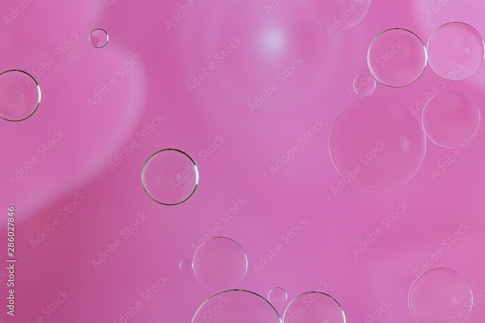 Close up oil drops floating on water surface with pink background