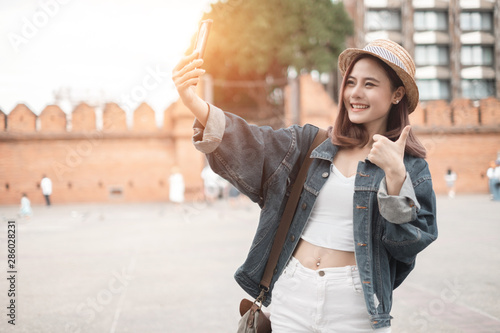 Smiling woman traveler in thapae gate landmark chiang mai thailand with backpack holding smartphone on holiday, relaxation concept, travel concept photo