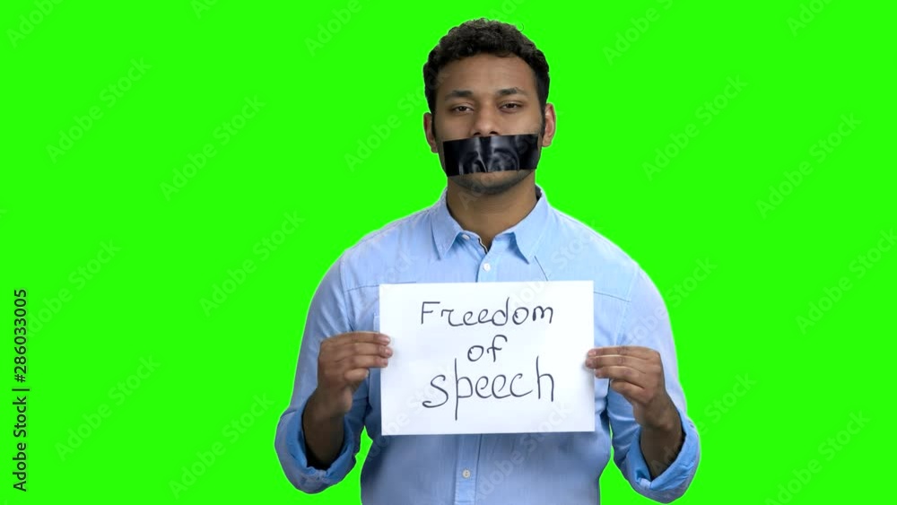 Young man with black tape on his mouth. Dark-skinned man with taped mouth and lips, green screen. Freedom of speech concept. Young man with black tape on his mouth. Dark-skinned man with taped mouth and lips, green screen. Freedom of speech concept.