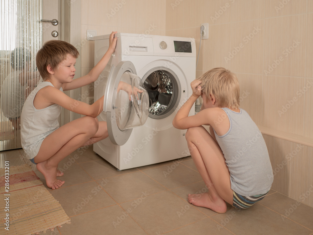 .Parents bought new washing machine of latest modification. Children try to turn it on and wash soft toys. Happy boys play at home. .Parents bought new washing machine of latest modification. Children try to turn it on and wash soft toys. Happy boys play at home.