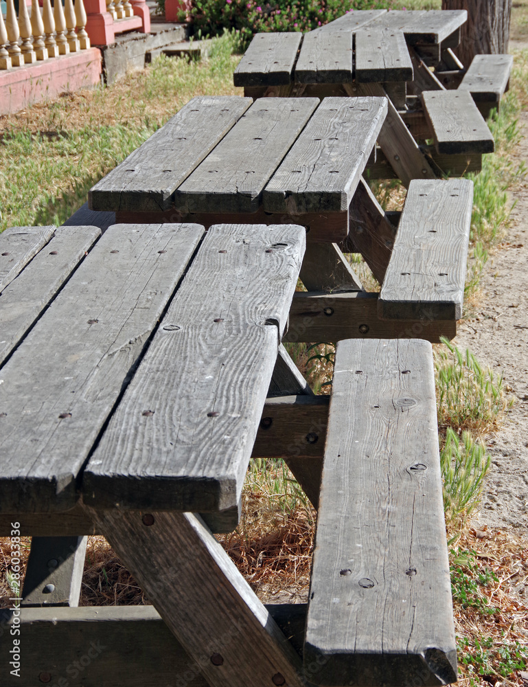 A row of rustic wooden picnic tables in a public park waiting to be used A row of rustic wooden picnic tables in a public park waiting to be used