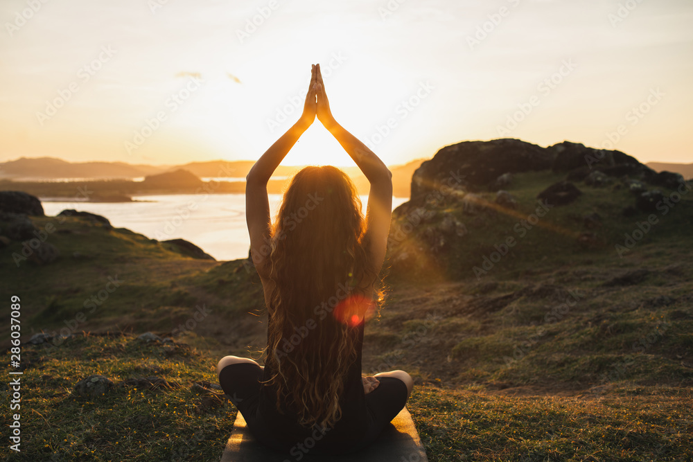 Young woman practicing yoga outdoors. Spiritual harmony, introspection and well-being concept. Landscape background - obrazy, fototapety, plakaty 