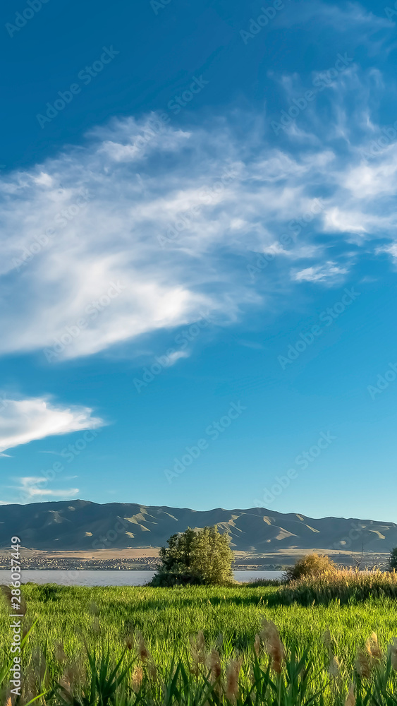 Obraz premium Vertical frame Nature scenery with a mountain towering over a calm lake viewed on a sunny day