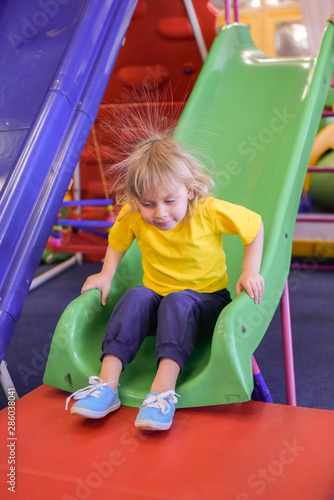 A boy riding on a hill. Portrait of a blond boy in a yellow t-shirt. The child smiles and plays in the children's playroom.