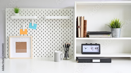 Workspace pegboard and shelves with office supplies on white office desk. photo