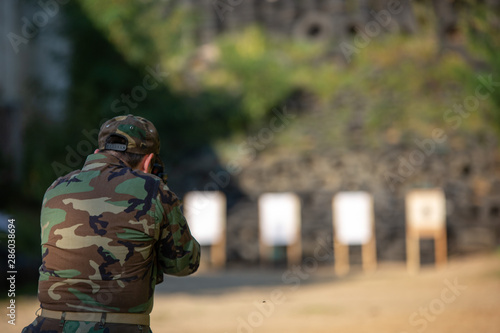 a guy in army clothes shoots at a target with a submachine gun