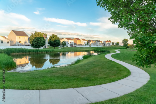 Photography Pathway and pond on a park covered with green grasses under blue sky with clouds