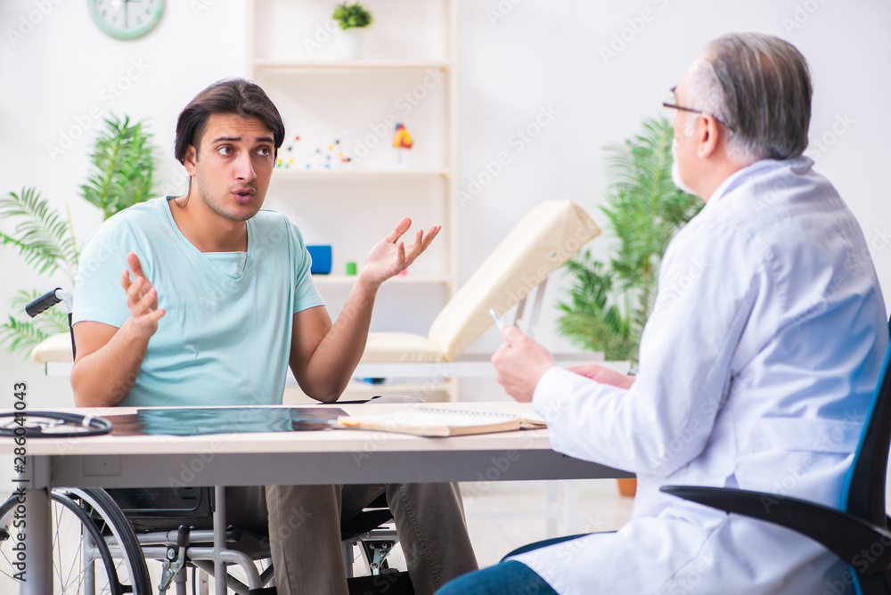 Fototapeta premium Male patient in wheel-chair visiting old doctor