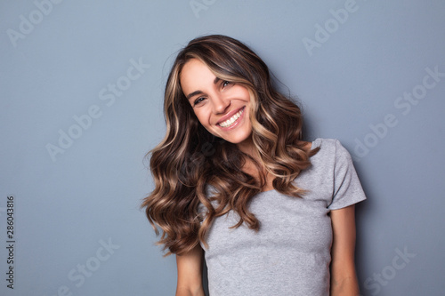 Smiling young woman on grey wall background.