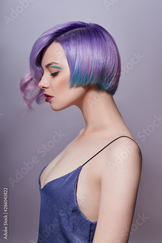 Portrait of a woman with bright colored flying hair, all shades of purple. Hair coloring, beautiful lips and makeup. Hair fluttering in the wind. Sexy girl with short hair. Professional coloring