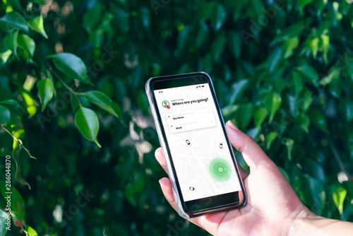 Hand holding mobile phone device outdoors to book taxi using ride hailing app - Woman booking internet taxi service using smartphone device for journey to work - cab, commuting and lifestyle concept