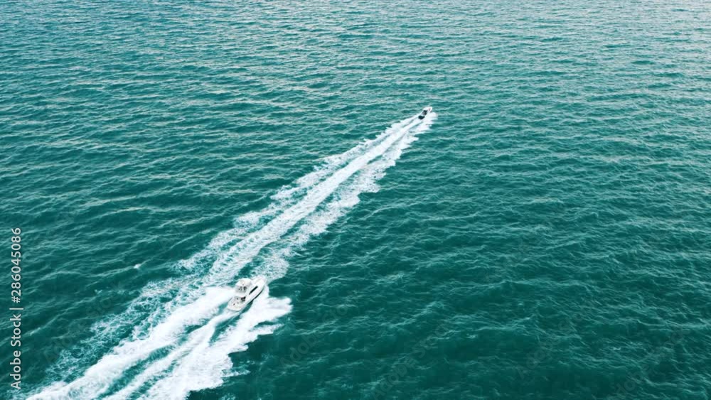 Trailing aerial view of two sport fishing boats chasing each other and hitting waves in open sea Trailing aerial view of two sport fishing boats chasing each other and hitting waves in open sea