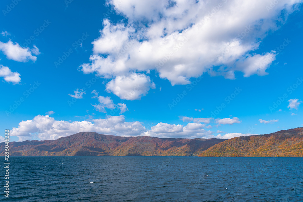 Beautiful autumn foliage scenery landscapes. Fall is full of magnificent colors. View from Lake Towada sightseeing Cruise ship. Clear blue sky, water, white cloud, sunny day background. Aomori, Japan Beautiful autumn foliage scenery landscapes. Fall is full of magnificent colors. View from Lake Towada sightseeing Cruise ship. Clear blue sky, water, white cloud, sunny day background. Aomori, Japan