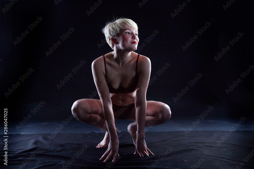 Sexy blonde girl during professional photo shoot in dark room. Model in a red swimsuit Sexy blonde girl during professional photo shoot in dark room. Model in a red swimsuit