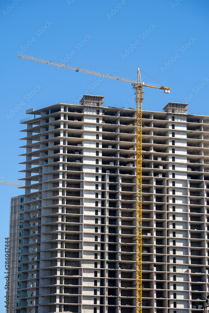 Construction of a high-rise building with a crane. The construction crane and the building against the blue sky.