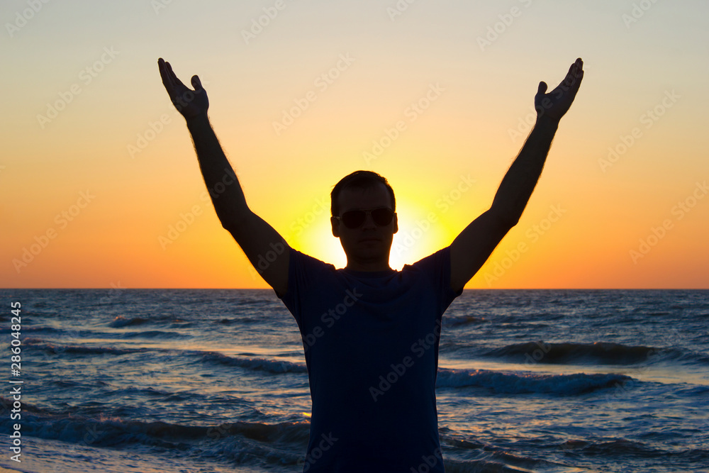 Fototapeta premium Young man hands up sunrise background blue sky and sea