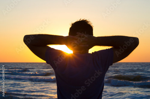 Young man hands behind head relax at sunrise sky sea